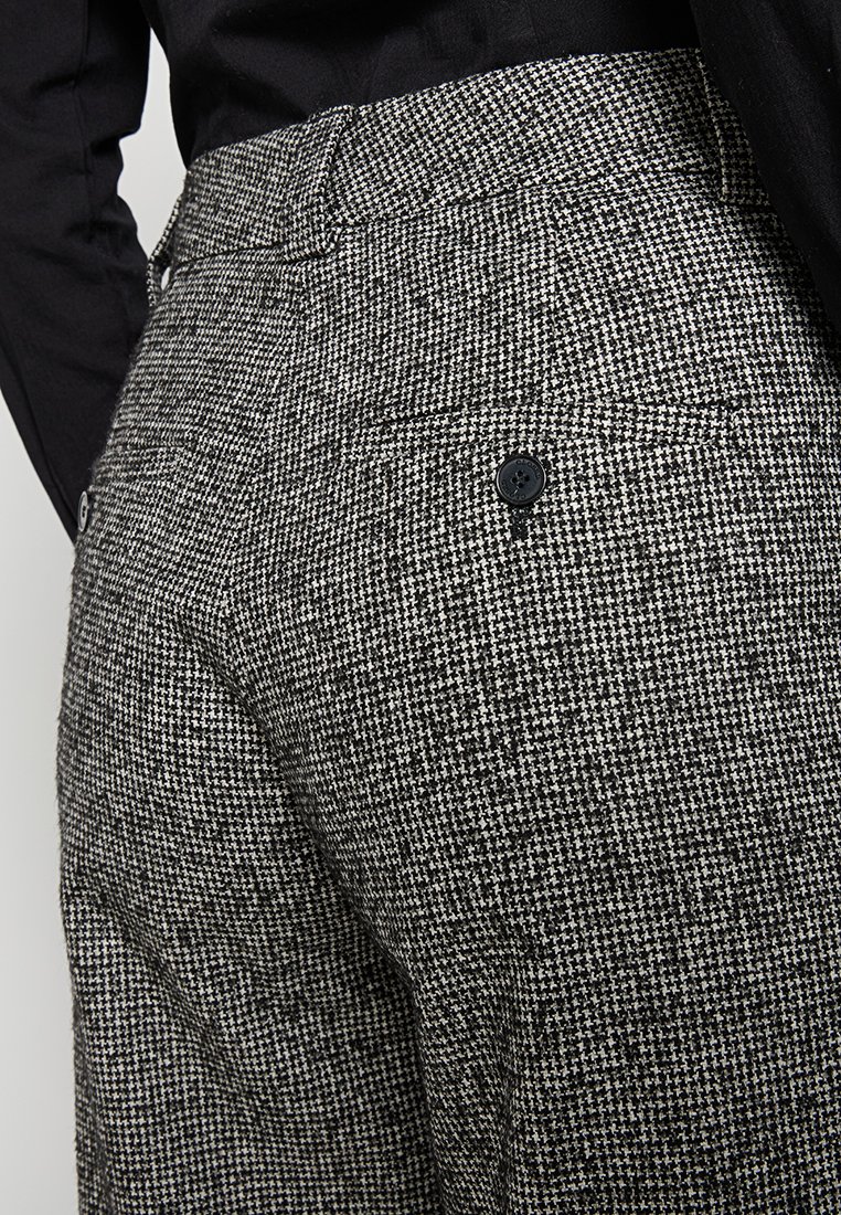 Maßgeschneiderte Hosen in einem schwarz-weißen Hahnentrittmuster, mit flachem Bund, Knopfdetails und glatter Textur.