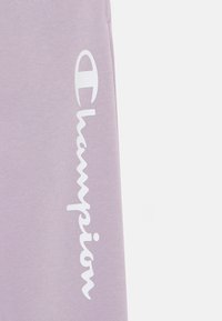 Lila sweatshirt med en texturerad tyg, med en framträdande vit "Champion"-logotyp tryckt vertikalt längs ärmen.