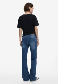 Musthave lühikeste varrukatega must t-särk paired tumedate siniste laienevate teksadega, mis sisaldavad seljataskuid ja nahast plaati vöökoha peal.