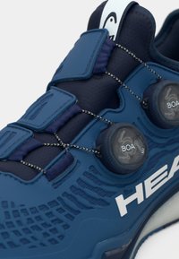 Modrá športová obuv s textúrovaným zvrškom, sieťovinovými panelmi a šnurovaním pomocou systému BOA. Na boku biele logo "HEAD" a gumová podrážka.