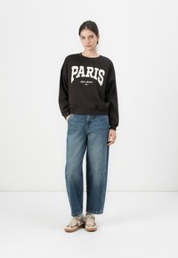 Black sweatshirt with "PARIS" text in cream, paired with light blue wide-leg jeans and beige sneakers. Simple, casual outfit design.