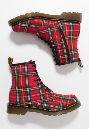 Paire de bottes à lacets à carreaux rouges avec fermetures éclair latérales et semelles épaisses translucides marron, montrées de côté et par dessous sur fond blanc.