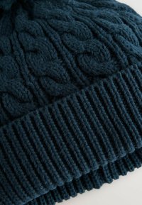Bonnet tricoté bleu foncé avec un design en relief et un ourlet côtelé. Fabriqué en fil épais et doux pour chaleur et confort.