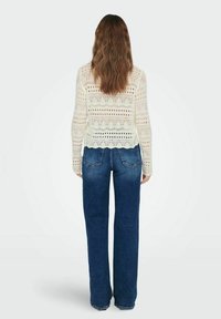 Top blanc en tricot à manches longues avec un motif ajouré et un ourlet festonné, associé à un jean flare bleu foncé taille haute.