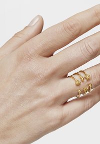 Gold rings in various shapes and textures are worn on a hand. The rings include spheres and decorative accents on thin bands.