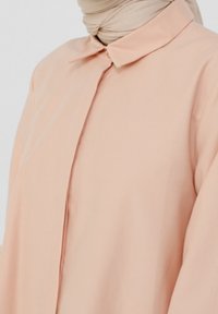 Blusa pesca chiaro con colletto, maniche lunghe e chiusura frontale a bottoni. Tessuto liscio e morbido con una vestibilità rilassata, dettagli di cucitura su misura.