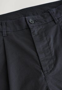 Pantalons légers noirs avec un devant plat, des poches latérales, un bouton de fermeture et une texture de tissu lisse. Coutures nettes et coupe ajustée.