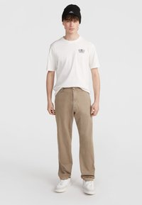 Hvid t-shirt med logo på brystet, khaki bukser med en afslappet pasform og hvide sneakers. Sort beanie fuldender det afslappede outfit.