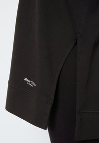 Camiseta negra de manga corta, con una abertura lateral, hecha de tela suave. Logo "Marc O’Polo" bordado en blanco en el dobladillo.