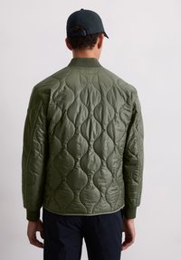 Gequilted olijfgroene jas met een gladde, glanzende afwerking. Voorzien van een staande kraag, ribgebreide manchetten en een onderscheidend patroon van afgeronde vormen.