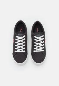 Baskets en toile noire avec lacets blancs, présentant une surface texturée et une semelle en caoutchouc. Comprend un petit logo Levi's rouge sur le côté.