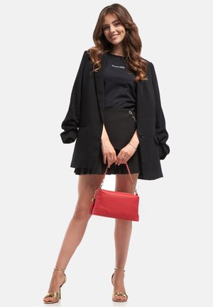 Blazer oversize nero, top fitted nero, mini gonna plissettata nera e sandali con cinturino dorati. Porta una borsa di pelle rossa con tracolla a catena.