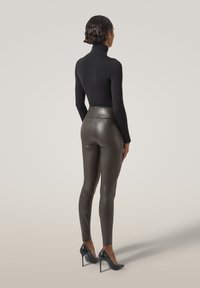 Svart polokrage topp tillsammans med metalliska, strukturerade leggings. Leggingsen har hög midja och kompletteras av svarta högklackade skor.