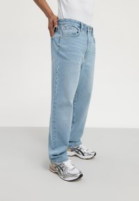 Blugi din denim de culoare albastru deschis, cu o croială lejeră, design cu cinci buzunare și cusături contrastante, asortați cu adidași argintii.