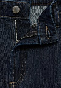 Tmavě modré džíny z denimu se zipem, viditelným prošíváním v kontrastní béžové barvě a stříbrným knoflíkem na pásku.