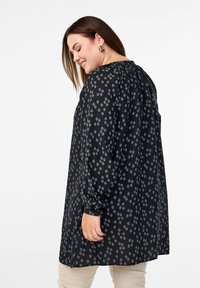 Blouse tunique noire avec motif en diamants blancs, manches longues, encolure froncée et coupe décontractée. Fabriquée en tissu léger au toucher doux.