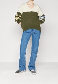 Sweter dzianinowy z dekoltem w serek, z kremową górną częścią i oliwkowozieloną dolną częścią. Paskowe, bufiaste rękawy w niebieskim i kremowym kolorze. Spodnie dzwony.