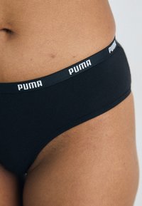 Culotte de bikini en coton noir avec une taille élastique arborant le logo "PUMA" en blanc. Texture lisse et design ajusté.