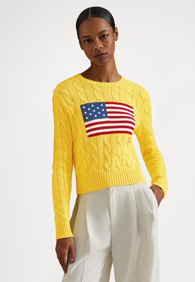 Rumeno pulover z vzorcem kabelskega tkanja, na sredini z motivom ameriške zastave. Rebrast izrez in manšete, krajši kroj. Mehka tekstura z izrazitim šivom.