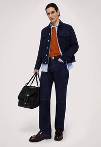 Marineblaue Cordjacke und Hose, oranger Pullover, hellblaues Hemd, schwarze Tasche und dunkle Schuhe mit glänzender Oberfläche. Einfaches Design und gerade Passform.