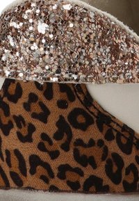 Sandalia de cuña marrón y dorada con parte superior de cuero brillante y sección inferior de tela con estampado de leopardo. Textura suave con un brillo sutil.