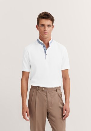 Weißes Poloshirt mit kurzen Ärmeln und blauem Kontrastkragen sowie zwei Knöpfen, kombiniert mit hellbraunen, gefalteten Hosen. Glatte Textur.