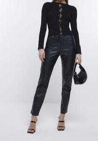 Svart ribbad tröja med snörning i fram och långa ärmar, kombinerad med högmidjade svarta byxor i konstläder och svarta heels med remmar.