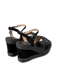 Sandali wedge neri con tomaia in suede testurizzato, arricchiti con dettagli lucidi. Presentano cinturini alla caviglia regolabili e una base in platform intrecciata.