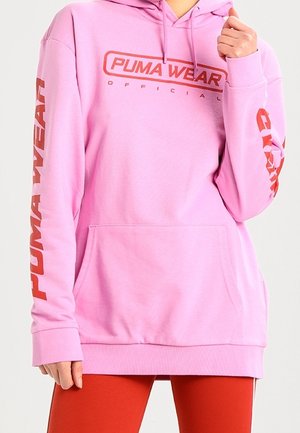 Sweatshirt à capuche rose avec une poche frontale, présentant le logo "PUMA WEAR" en rouge sur la poitrine et la manche gauche. Texture de tissu douce.