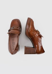 Zapatos de charol marrón con un tacón grueso y una correa decorativa cruzando el empeine, que presentan una sutil textura de vetas de madera en el tacón.