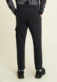 Pantalones de chándal negros hechos de una tela suave, con un corte ajustado, cintura elástica y bolsillos laterales. Combinados con zapatillas deportivas negras.