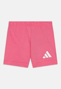Rozā sporta šorti, izgatavoti no mīkstas auduma, ar elastīgu jostu un baltu Adidas logo apakšējā kreisajā stūrī.