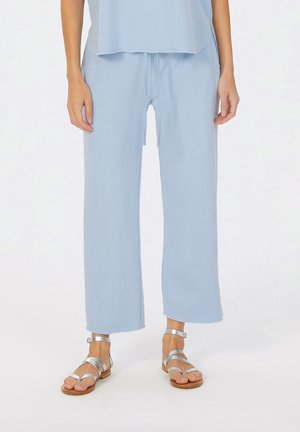 Light blue loose-fitting pants with a drawstring waist, cropped length, and soft texture, paired with silver strappy sandals.