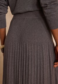 Gonna grigia plissettata con costine verticali, tessuto strutturato, vita alta e finitura liscia. Vista ravvicinata della sezione posteriore e dettaglio del tessuto.
