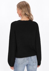 Puloverul negru pufos are guler rotund și mâneci lungi, ușor evazate. Designul prezintă o croială scurtă și o textură moale.