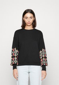 Sweatshirt preto com bordados geométricos coloridos nas mangas, gola redonda e punhos canelados. Material de algodão macio, corte relaxado.