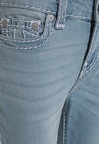 Světle modré džíny z denimu mají kontrastní bílé švy, přední kapsu s knoflíkovými akcenty a střih s rovnými nohavicemi.