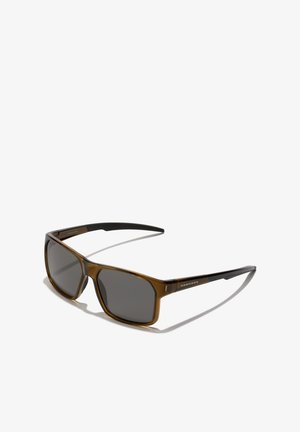 Lunettes de soleil en plastique transparent marron avec des verres gris foncé, présentant une forme de monture rectangulaire et des branches texturées noires.