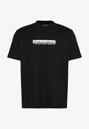 Sort kortærmet t-shirt med en hvid rektangulær etiket tværs over brystet med teksten "Calvin Klein" i sort.