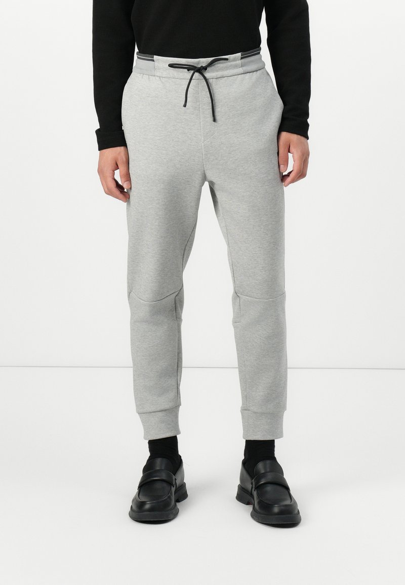 Grå joggebukser med ribbestrikket liv og justerbar snor. Har smale ben og teksturert stoff. Stylet med svarte loafers.