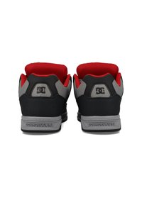 Černé a šedé tenisky s červenými akcenty, které mají polstrovaný límec, texturovanou tkaninu a detail loga na patě.