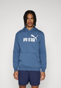 Blauer Hoodie aus weichem Material, mit einem großen weißen "PUMA"-Logo und einer Kängurutasche, mit Kapuze mit Kordelzug und gerippten Bündchen.