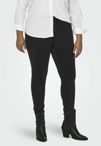 Black skinny jeans made from denim, featuring a high waist, subtle texture, and slim fit, paired with black heeled ankle boots.