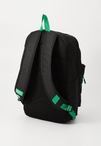 Black fabric backpack with green accent straps. Features padded mesh backing and exterior pockets. Zippered compartments for storage.