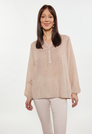 Blusa lunga a maniche con colletto a V in lino beige chiaro, con patta a quattro bottoni e polsini arricciati. Abbinata a pantaloni fitted beige chiaro.