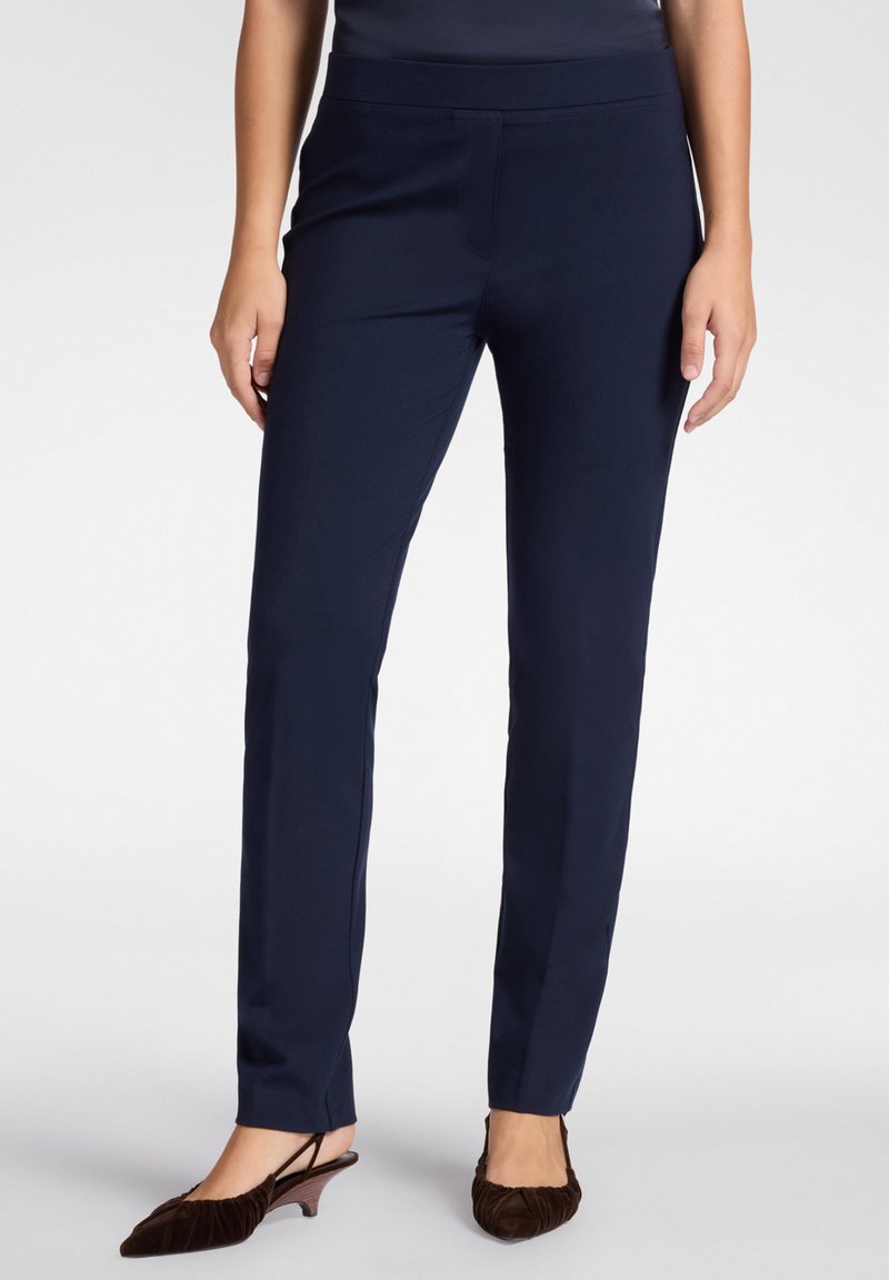 Pantalones azul marino a medida con una suave cinturilla elástica, diseño ajustado y una silueta elegante, combinados con unos zapatos de tacón tipo slingback marrones y texturizados.