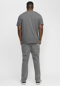 Graues Baumwoll-T-Shirt mit Rundhalsausschnitt, kombiniert mit hellgrauen Hosen mit Gesäßtaschen. Das Modell trägt schwarz-weiße Sneakers.