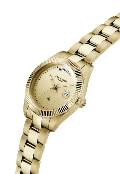 Goudkleurig metalen polshorloge met gesatineerde bezel, dag- en datumvensters die maandag en 28 tonen, en een geborsteld wijzerplaat met de handtekening "rag & bone."