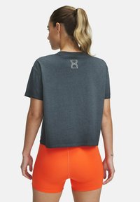Camiseta gris cortada con un logo impreso en la parte posterior, combinada con pantalones cortos de un vibrante color naranja. El material parece suave; el diseño es simple y deportivo.