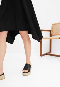 Černé šaty s vysokým a nízkým lemem, s žebrovanou texturou. Nosit s černými skluznými sandály s širokým páskem a tkaným jutovým podpatkem.